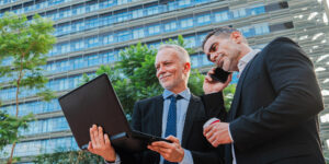 Gestores analisando informações em notebook e falando ao celular, representando tomada de decisão integrada na gestão do condomínio
